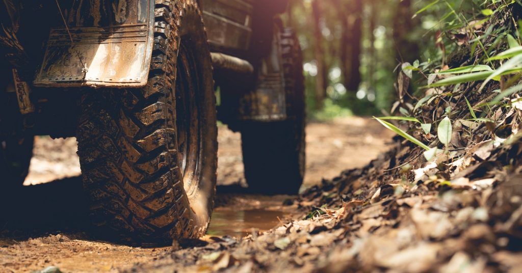 An off-roading vehicle sitting on a dirt forest road. Mud covers the tires and the lower half of the vehicle.