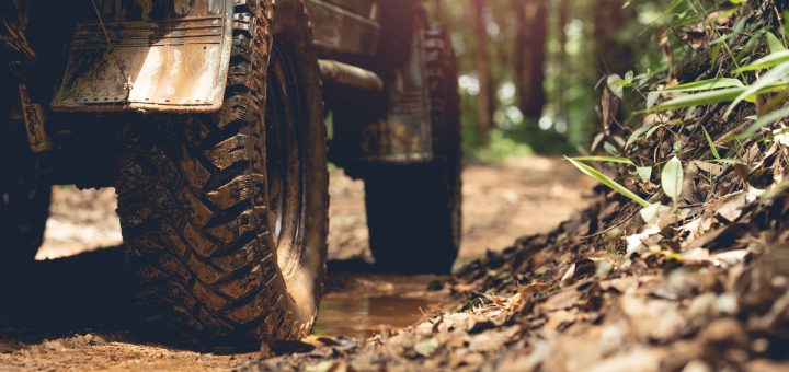 An off-roading vehicle sitting on a dirt forest road. Mud covers the tires and the lower half of the vehicle.
