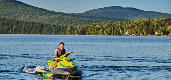 A rookie jet skier wears a safety vest on the lake on a sunny afternoon. They're going slow and the water is calm.