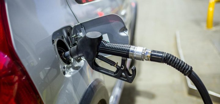 Close-up of a silver car refueling at a gas station with the fuel nozzle inserted and background softly blurred.