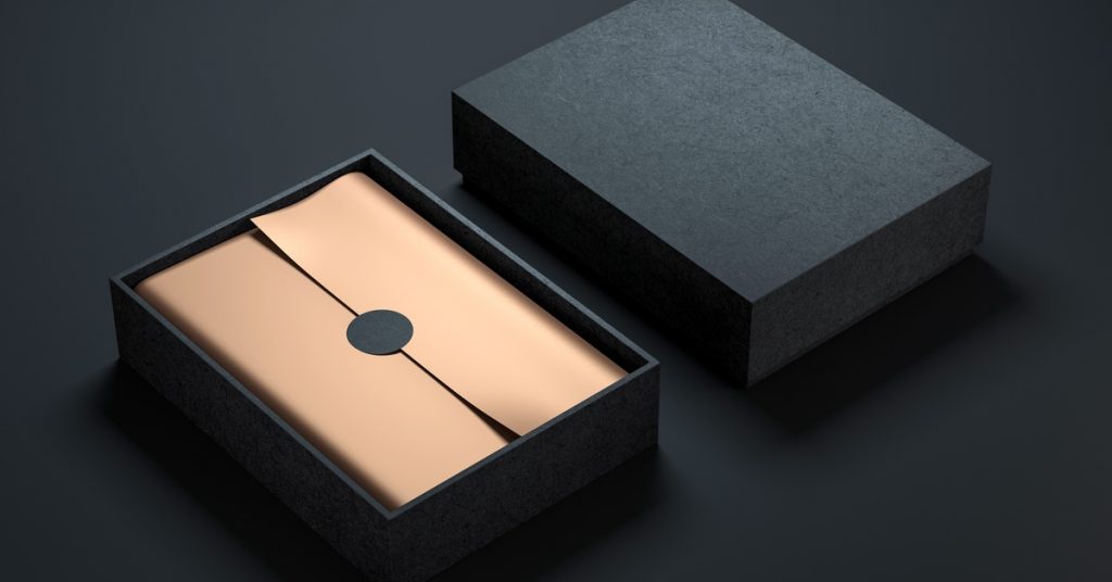 A black rigid box with the top next to the bottom part of the package. Inside is gold paper with a black circle sticker in the center
