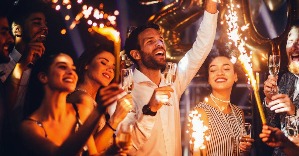 A group of friends with beverages and sparklers ringing in the new year together with smiles on their faces.