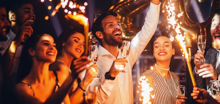 A group of friends with beverages and sparklers ringing in the new year together with smiles on their faces.