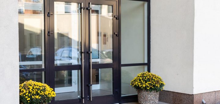 A glass entrance door of an office building with two flower pots of yellow flowers placed on either side of the doorway.