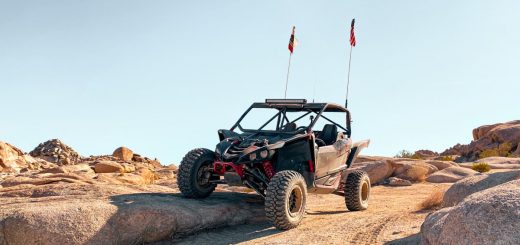 A dirt-covered side-by-side UTV on an off-road trail. One of its wheels is elevated onto a nearby rock.