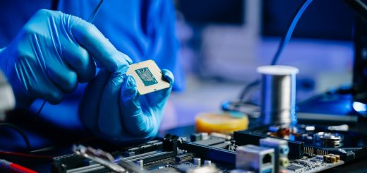 An engineer sits at their workstation as they wear blue latex gloves to hold and work on a microchip for an electronic.