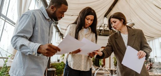 Three people holding paper documents in an event venue. The group looks at one of the documents together.