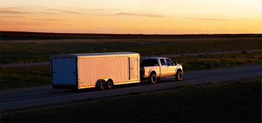 A pickup truck traveling down a country road as the sun sets. There's a travel trailer hooked up to the truck.