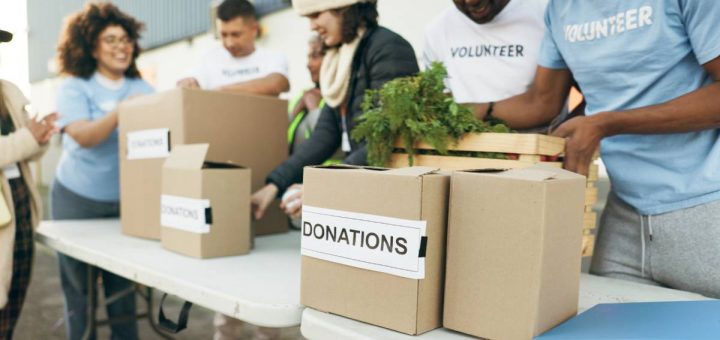People standing behind a table, wearing shirts that say "volunteer." Boxes line the table labeled "donations."