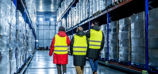 Three team members wearing heavy jackets under neon-yellow safety vests are walking in a warehouse.