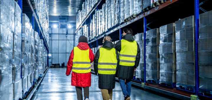 Three team members wearing heavy jackets under neon-yellow safety vests are walking in a warehouse.