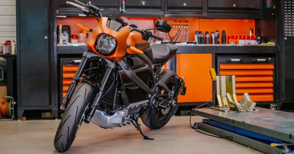 A close-up of an orange and black motorcycle in a garage with black and orange storage cabinets. There is a lift by the bike.