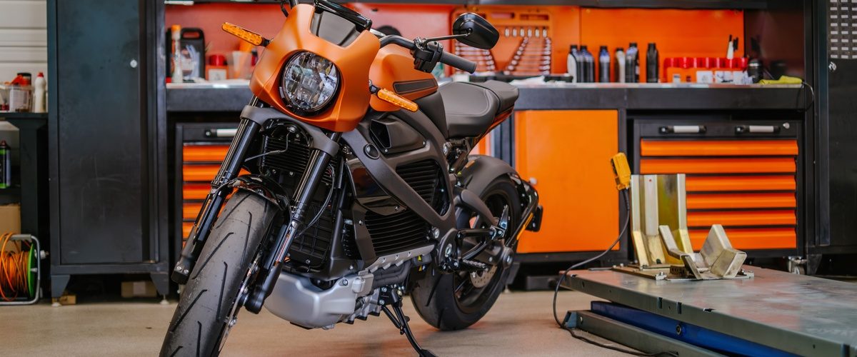 A close-up of an orange and black motorcycle in a garage with black and orange storage cabinets. There is a lift by the bike.