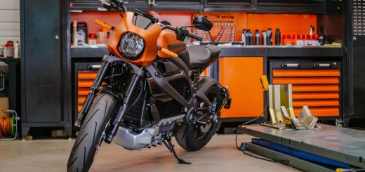 A close-up of an orange and black motorcycle in a garage with black and orange storage cabinets. There is a lift by the bike.