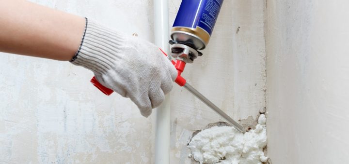 A person is holding a spray foam gun and is using it to install foam into a crack on a concrete wall.