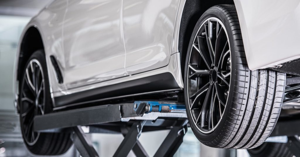 A white vehicle lifted in a repair shop with the driver's side tires exposed. The tires appear brand-new.