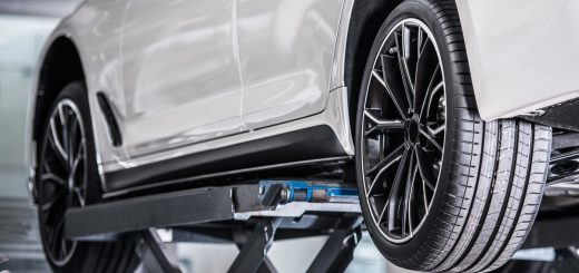 A white vehicle lifted in a repair shop with the driver's side tires exposed. The tires appear brand-new.