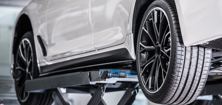 A white vehicle lifted in a repair shop with the driver's side tires exposed. The tires appear brand-new.