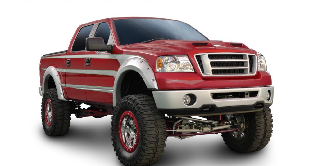 A red truck with silver trim is parked against a solid white background. The truck is clearly lifted with a greater height.