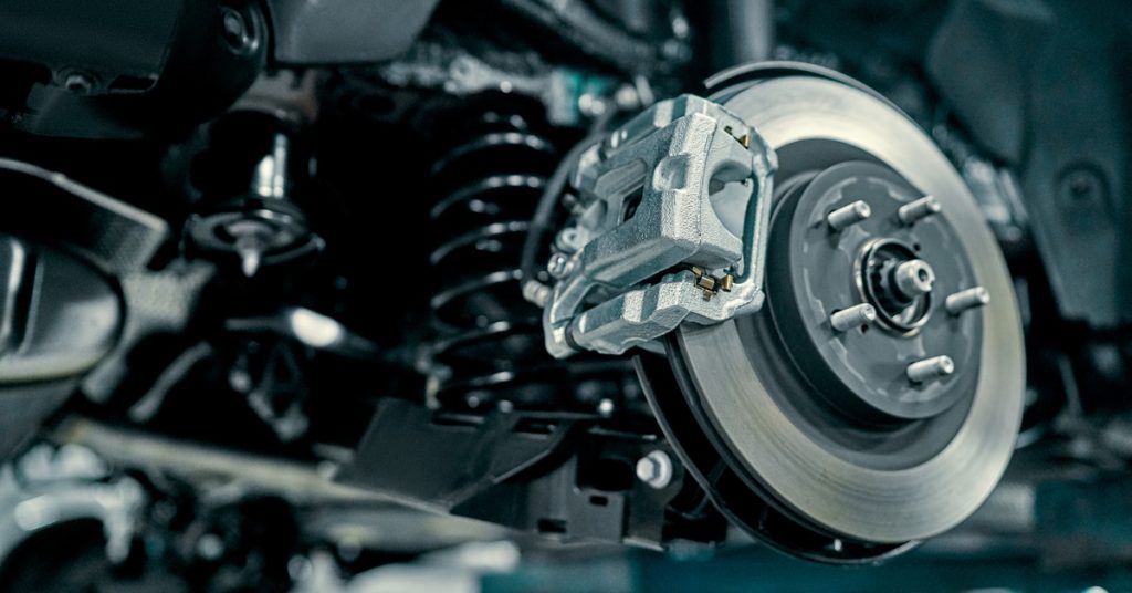A vehicle disc brake and caliper exposed beside suspension parts while undergoing repair in an automotive garage.