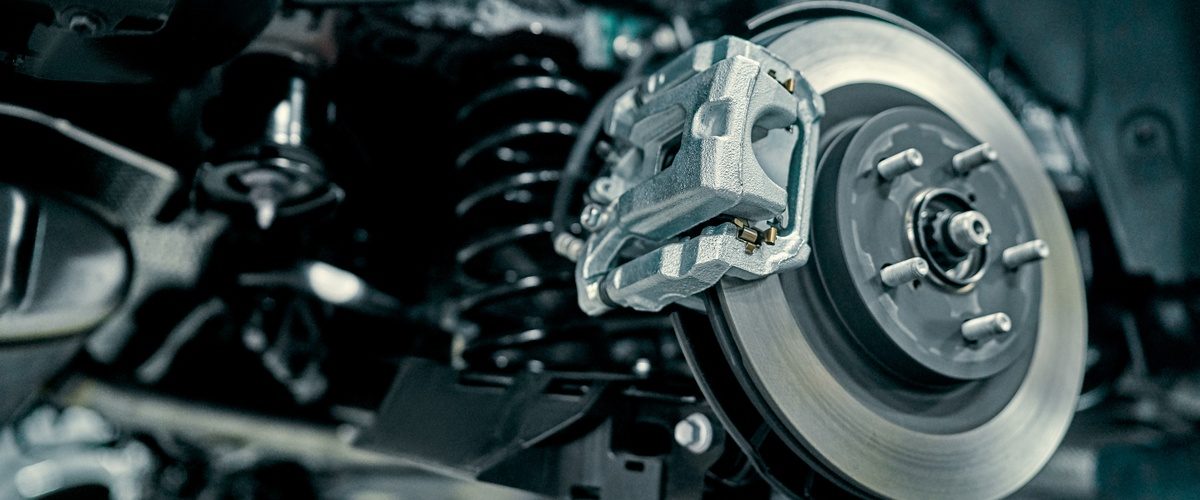 A vehicle disc brake and caliper exposed beside suspension parts while undergoing repair in an automotive garage.