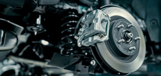 A vehicle disc brake and caliper exposed beside suspension parts while undergoing repair in an automotive garage.