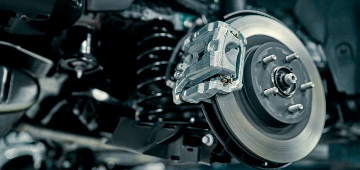 A vehicle disc brake and caliper exposed beside suspension parts while undergoing repair in an automotive garage.