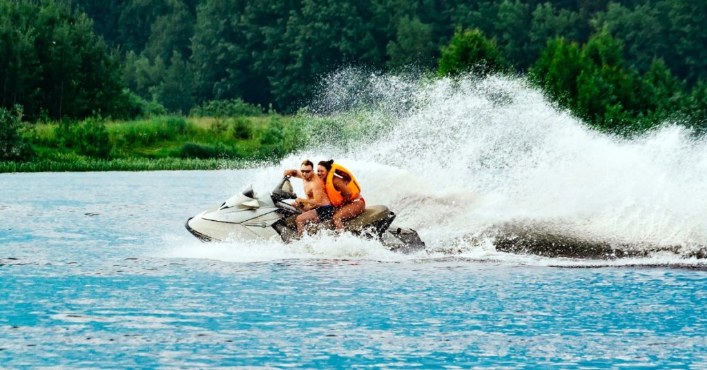 Two people riding a personal watercraft across the water and leaving a trail of large waves behind them.