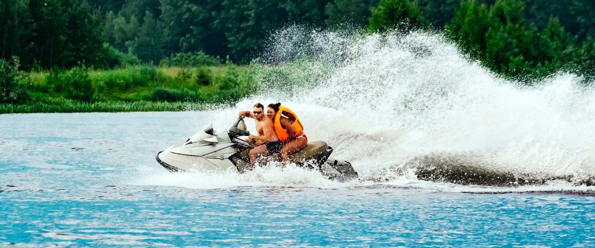 Two people riding a personal watercraft across the water and leaving a trail of large waves behind them.