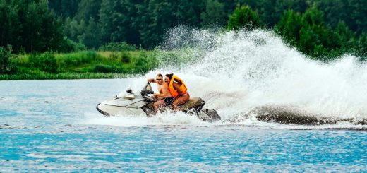 Two people riding a personal watercraft across the water and leaving a trail of large waves behind them.