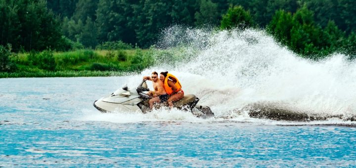 Two people riding a personal watercraft across the water and leaving a trail of large waves behind them.