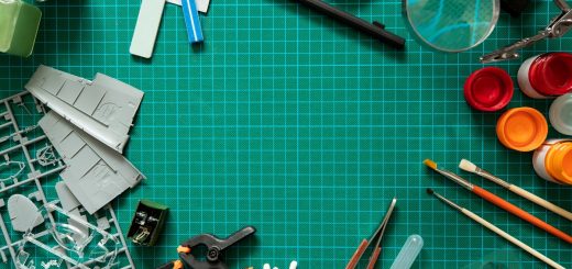An overhead view of various hobby tools like paintbrushes, blades, and rulers on a green cutting mat.