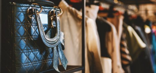 A close-up of a black leather bag with gold hardware placed on a shelf next to a clothing rack with multiple items.