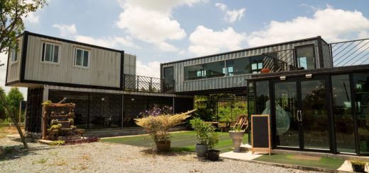 Modern building built from stacked shipping containers with large windows, glass entryway, patio plants, and open courtyard.