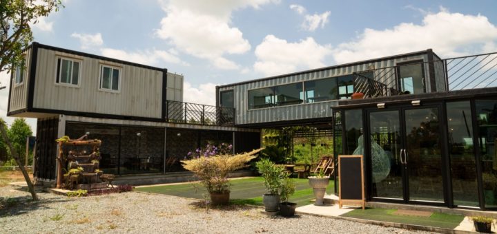 Modern building built from stacked shipping containers with large windows, glass entryway, patio plants, and open courtyard.