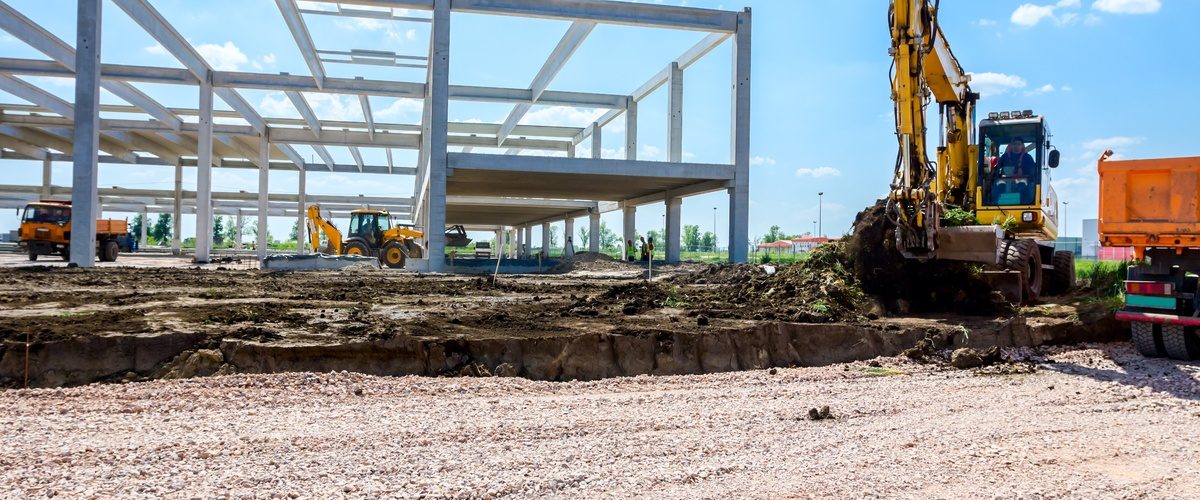 The frame of a building is built in the middle of an empty field. There is a large piece of machinery next to the frame.