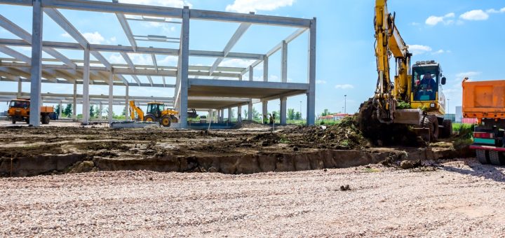 The frame of a building is built in the middle of an empty field. There is a large piece of machinery next to the frame.