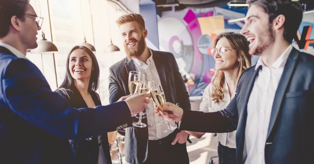 A group of five business professionals standing in a circle talking and clinking their wine glasses together.