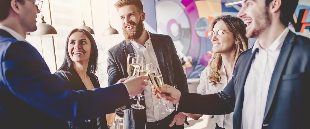 A group of five business professionals standing in a circle talking and clinking their wine glasses together.