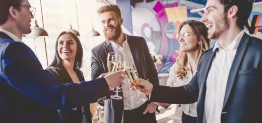 A group of five business professionals standing in a circle talking and clinking their wine glasses together.