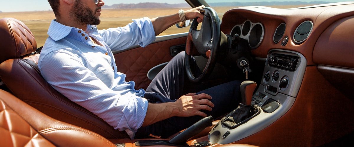  Person drives a luxury convertible with quilted leather seats across an open desert beneath a clear blue sky.