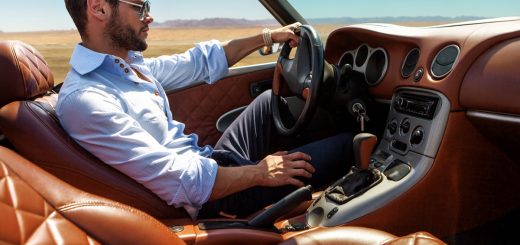  Person drives a luxury convertible with quilted leather seats across an open desert beneath a clear blue sky.