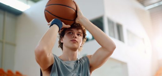 A close-up of a young man standing in a gym. He holds a basketball up near his forehead, ready to shoot a basket.