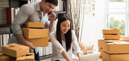 A man holding packages while on the phone as a woman works on a laptop surrounded by shipping boxes.