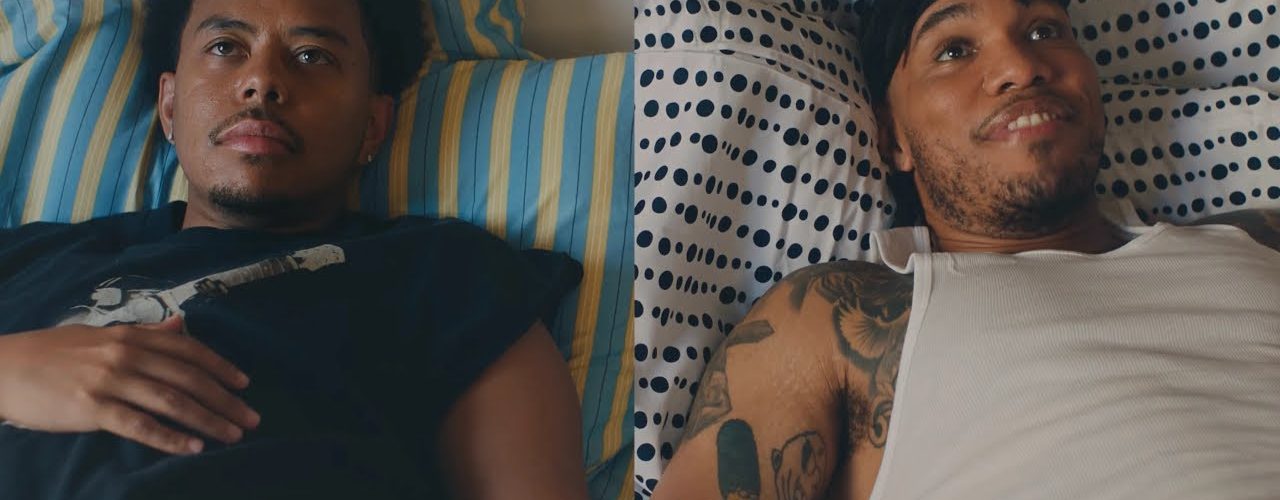 "Cordae and Anderson .Paak lying in bed in split-screen still from 'A Good Day' music video"