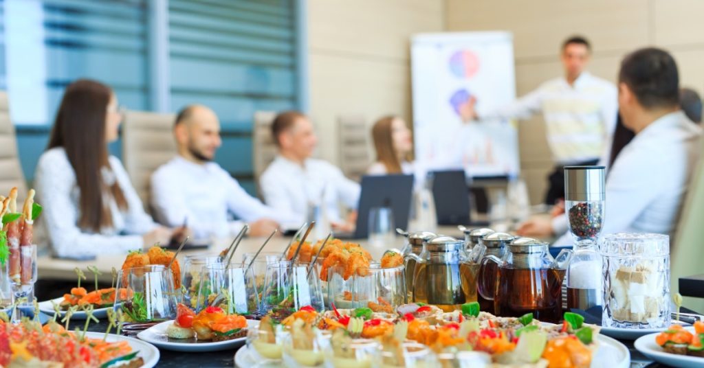 A close-up of a table in a business office meeting room filled with catered finger foods and drinks.