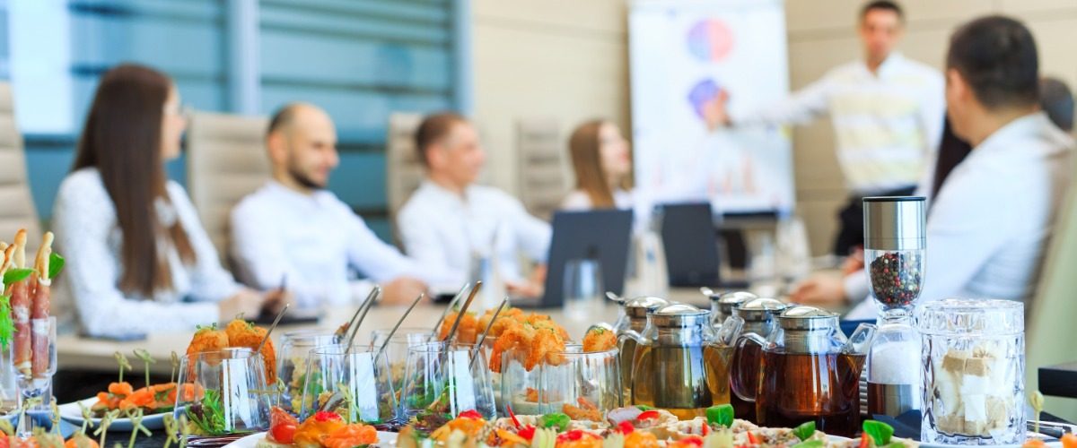 A close-up of a table in a business office meeting room filled with catered finger foods and drinks.