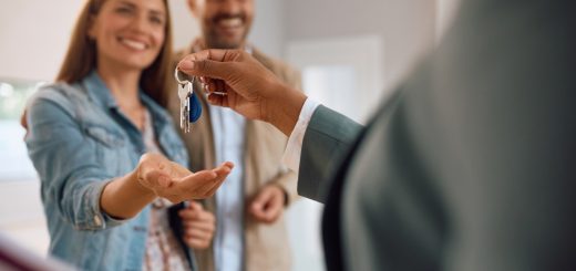 A close-up of the hand of a person holding a set of keys over the hand of a woman standing next to a man in a room.