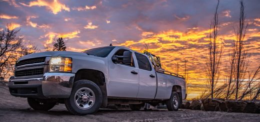 A white heavy-duty diesel pickup truck parked on rough terrain beneath a dramatic orange and purple sunset sky.