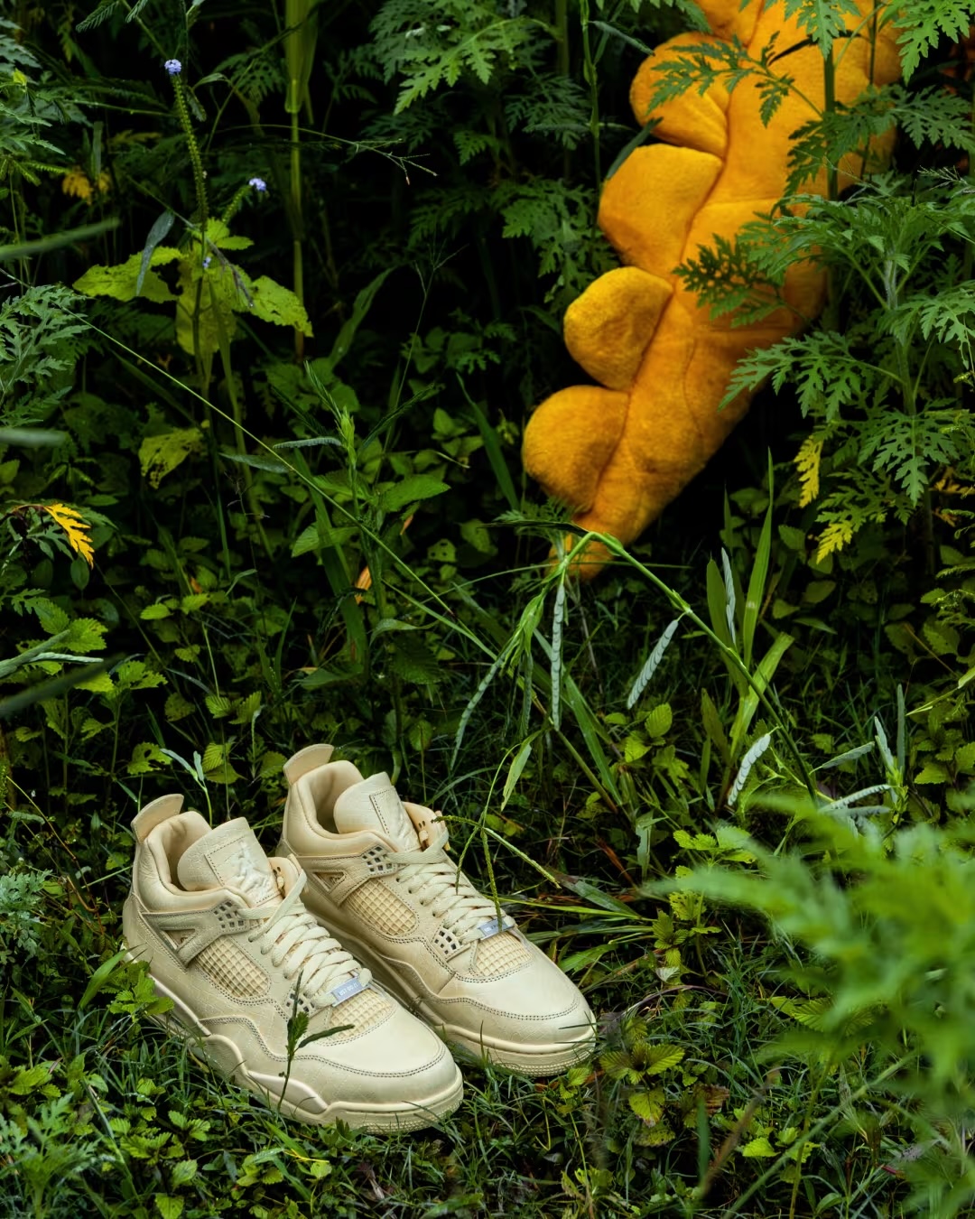 Pair of Air Jordan 4 x J Balvin sneakers staged outdoors among greenery and carrots